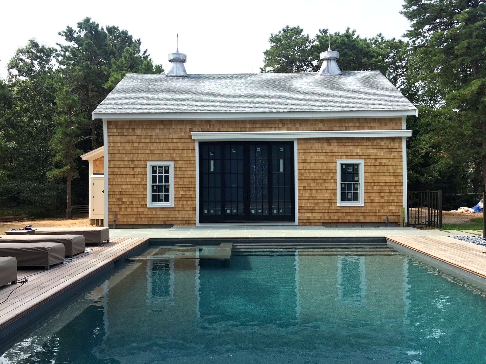Cedar shake pool house with four-panel sliding glass door, white trim, and cupolas on Cape Cod